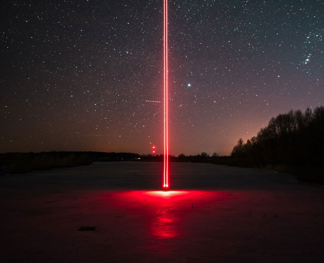 Paisaje de noche en el que sale de la tierra hacia el cielo un rayo láser rojo